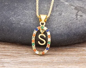 Close-up detail of a gold-plated necklace featuring a colorful zircon oval pendant and letter S.