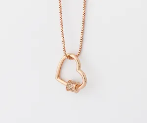 Gros plan du pendentif de collier cœur en or rose avec zirconiums micropavés.