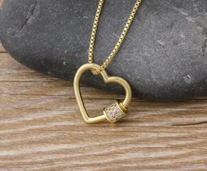 Gros plan detail d'un collier pendentif mousqueton coeur dore sur fond de pierre noire.