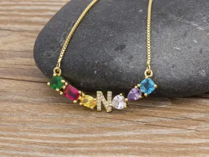 Close-up detail of the colorful zircon letter N pendant necklace on stone and wood.