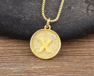 Gold plated initial X pendant necklace with sparkling zirconia on textured round coin charm.