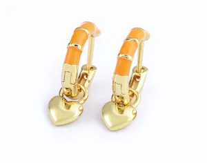 Close-up detail of gold hoop earrings with orange enamel and dangling heart charms.