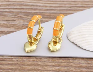 Close-up detail of trendy orange enamel bamboo hoop earrings with cute dangling gold hearts.