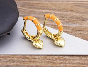 Close-up detail of the orange enamel bamboo hoop earrings with cute heart charms in gold.