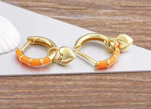 Close-up detail of 18k gold plated copper hoop earrings with orange enamel and heart charm.