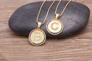 Close-up of gold initial letter pendants with sparkling rainbow zircon stones on smooth stone.