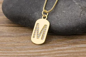 Gold letter M pendant necklace detail, sparkling zircon pavé dog tag on delicate box chain.