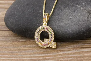 Close-up detail of the gold letter Q pendant featuring colorful zirconia stones on a dark stone.