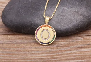 Gold letter O pendant necklace with colorful cubic zirconia stones on stone background detail.