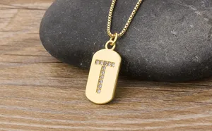 Detail shot of a gold-plated initial letter T pendant necklace with sparkling zircon stones on pebble.