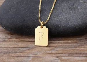 Primo piano dettagliato di una collana con ciondolo lettera F quadrata dorata su pietra.