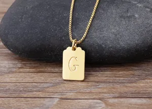 Dettaglio collana con ciondolo quadrato placcato oro, gioiello alfabeto G minimalista.