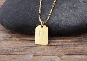 Primo piano dettaglio di una collana con ciondolo quadrato lettera H placcato oro.