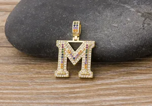 Detailed close up view of gold plated letter M pendant sparkling with colorful zirconia stones.