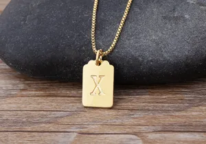Primo piano di un ciondolo quadrato dorato minimalista con incisione dettagliata della lettera X.