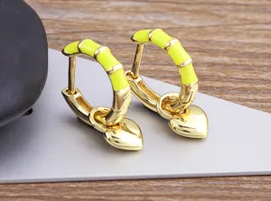 Neon yellow enamel bamboo hoop earrings with dangling gold heart pendant, detailed shot.