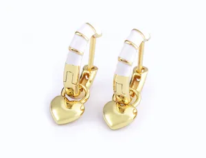 Close-up of gold-plated hoop earrings with white enamel details and cute heart pendants.