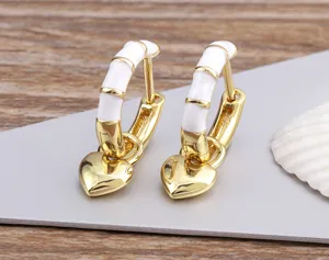 Close-up detail of golden hoop earrings with white enamel bamboo segments and cute heart charms.