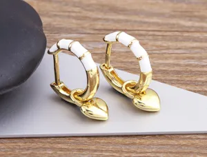 Detail shot of gold hoop earrings with white enamel segments and cute dangling heart charms.