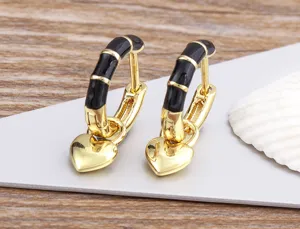 Detailed close-up of gold-plated hoop earrings with black enamel and a dangling heart pendant.