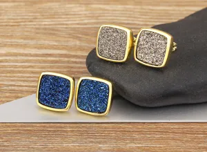 Close-up detail of square druzy stud earrings in blue and bronze with gold metal frame.