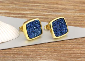 Detailed close-up of square gold-rimmed blue crystal druzy stud earrings on stylish display.