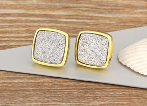 Close-up view of elegant square stud earrings featuring sparkly center and gold tone frame.