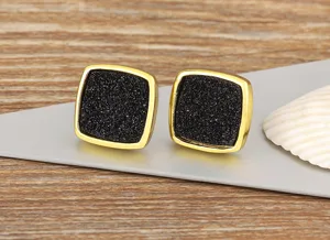 Close-up of vintage square black druzy stud earrings with gold rim on metallic display prop.