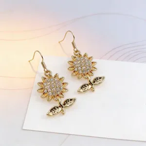 Close-up detail of shiny rhinestone sunflower drop earrings with gold finish and leaf accents.
