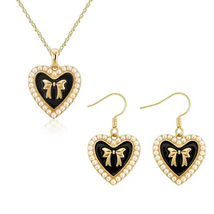 Gold-tone heart necklace earrings set featuring black enamel, pearl border, and bow detail.