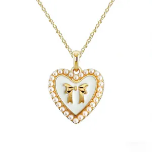 Gold heart pendant necklace featuring white enamel bow and elegant faux pearl border design.
