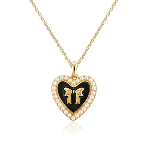 Close-up detail of the gold-tone heart pendant necklace with black enamel, bow, and faux pearls.