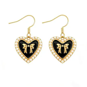 Detailed close-up of gold hook earrings featuring black heart pendant with faux pearls and bow.