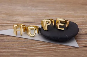 Close up detail of gold plated alphabet letter rings featuring HOPE design, open ring style.