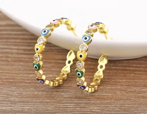 Close-up of gold-plated hoop earrings featuring colorful enamel evil eyes and cubic zirconia.