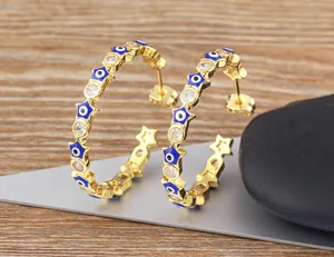 Close-up detail of gold evil eye star hoop earrings with clear zircon stones and blue enamel.