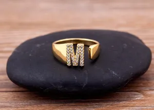 Close-up of gold-plated open letter M ring featuring sparkling cubic zirconia details on stone.