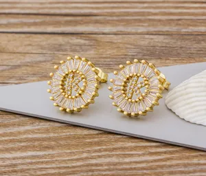 Primer plano detalle de pendientes de boton letra K dorados con circonitas baguette brillantes.