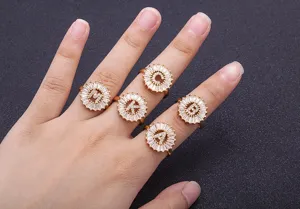 Detailed close-up shot of gold plated alphabet zirconia rings worn on hand, elegant design.