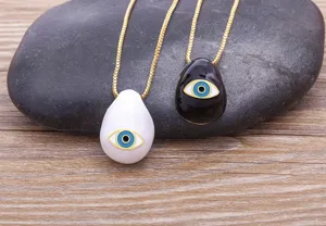 Detailed view of stylish teardrop evil eye pendants in black and white with gold chains.