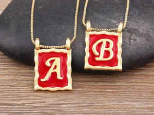 Detailed shot of gold-plated square letter pendant necklace with red enamel design.