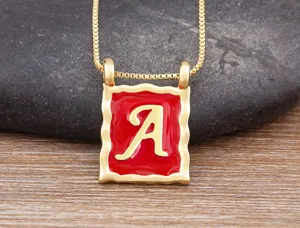 Close-up of gold plated square letter A pendant necklace with red enamel and chain details.