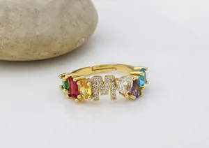 Primo piano dettagliato di un anello placcato oro con zirconi colorati e lettera M.