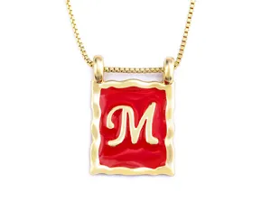Detail view of the gold-plated square pendant necklace featuring a bold letter M in red enamel.