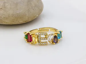 Primo piano dell'anello in rame placcato oro 18k con zirconi multicolori e lettera E.