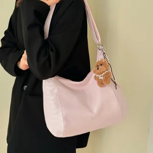 Pink hobo shoulder bag with stylish plush bear keychain and chic side pattern details.