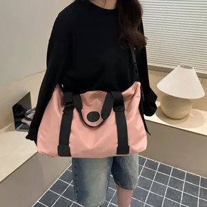 Detailed close-up view of a casual pink travel duffel bag with black straps, worn by model.