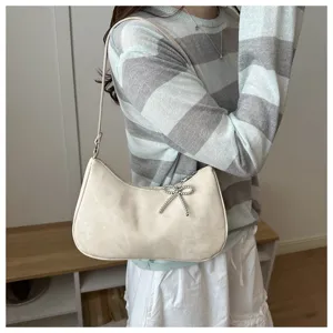 Chic beige shoulder bag with sparkling beaded bow pendant, stylish underarm design for women.