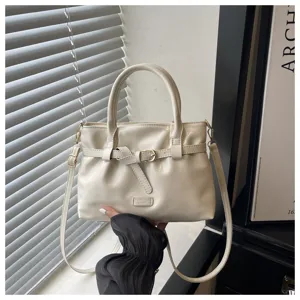 Detail view of simple solid color women handbag with belt decoration and shoulder strap in cream.