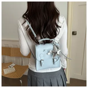 Detail view of light blue polka dot backpack with star pendant, bow, and dual buckle straps.